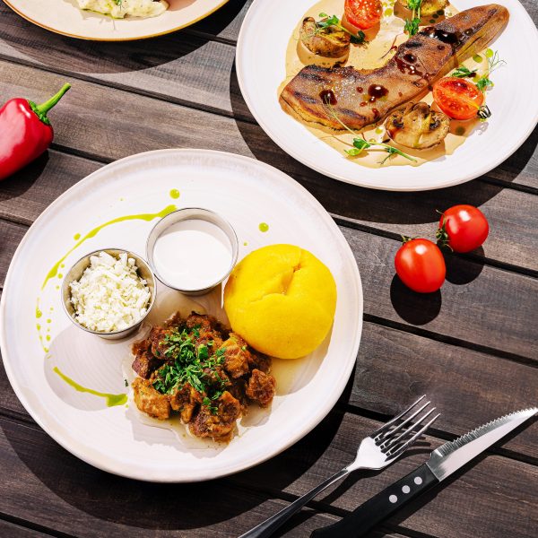 A beautifully presented plate features tender meat, yellow corn dough, and fresh vegetables. The rustic table enhances the inviting atmosphere of a midday dining experience.